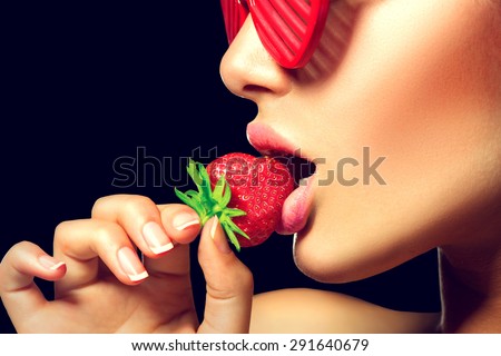Sexy Woman wearing glamour red sunglasses Eating Strawberry. Sensual Red Lips. Desire. Sexy Lips with Strawberry. Isolated on black background
