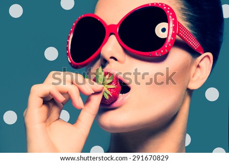 Sexy Woman in Big red Sunglasses Eating Strawberry. Sensual Lips. Manicure and Lipstick. Desire. Sexy red Lips with Strawberry. Retro styled Fashion girl over polka dots background