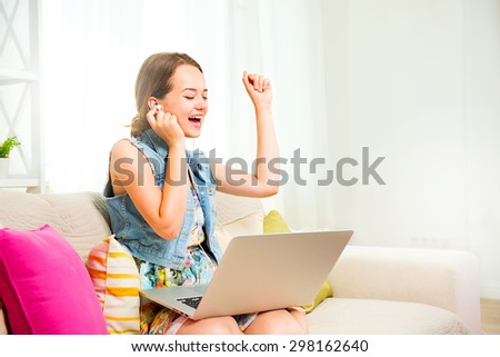 Pretty teenage girl sitting on sofa at home with laptop computer, listening music with headphones and dancing. Emotions