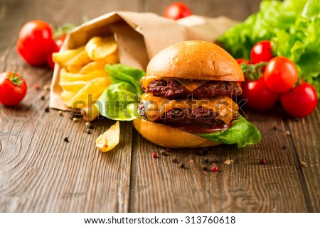 Juicy and fragrant hamburger with fried potatoes on rustic wooden surface. Cheeseburger with tasty buns and juicy meet cutlet with fresh vegetables served with French Fries on a dark wooden table.
