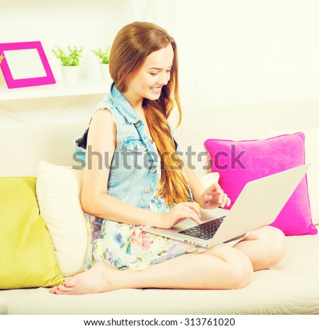 Pretty teenage girl sitting on sofa at home with laptop. Happy Girl with long hear typing on laptop and smiled. Teenage girl using laptop computer