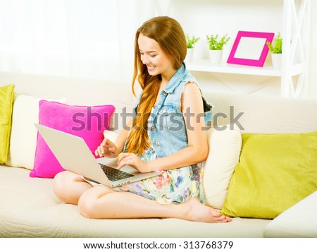 Pretty teenage girl sitting on sofa at home with her laptop, making thumb up gesture. Beauty girl enjoying the networks by laptop computer, laughing student.