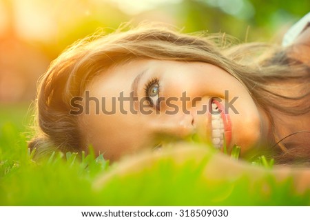 Beauty teenage Romantic Girl lying on the grass close-up. Outdoors. Brunette Model girl with blue eyes smiling and enjoying nature. Cute Teenage Girl lying on grass. Grassland. Sunshine