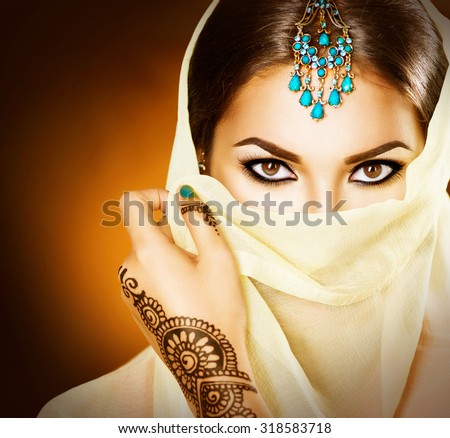 Beautiful Arabian girl portrait. Young Hindu woman with mehndi tattoos from black henna on her hands. Portrait of beauty Indian model with bright make-up who hiding her face behind the veil
