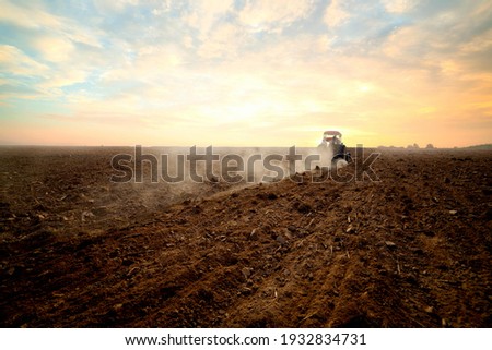 Agriculture use tractor plowing land field in the backround. Cultivated field. Agronomy, farming, husbandry .Tractor working on farm at sunset,modern agricultural transport,farmer working in the field 商業照片 © 