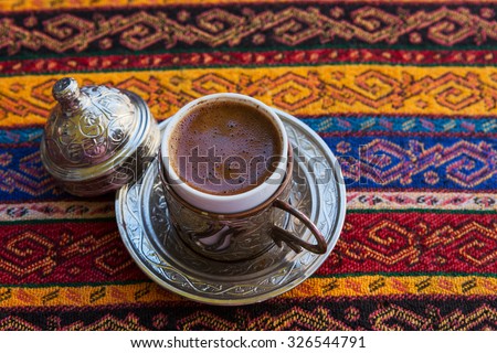 Traditional Turkish Coffee in a ceramic coffee mug covered with copper pot on tablecloth traditional texture and pattern