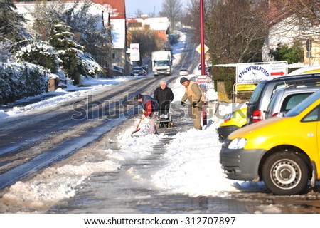 Worms, Germany - December 9, 2010: Old woman walking on snowy road while public workers cleaning walkway