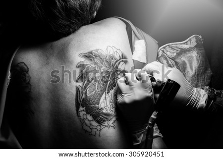 Showing process of making a tattoo by female artist. Tattoo design in fish pattern.