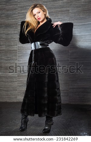Fashion beautiful blonde woman posing in fur coat. Winter Girl Model in Luxury clothes and furry collar on gray background.