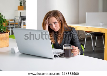 Depressed businesswoman sitting at computer. Tired and sleepy office worker looking at the laptop screen and needs help