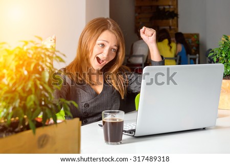 Excited happy businesswoman with raised arms sitting at the table with laptop celebrating her success. Green eco office concept