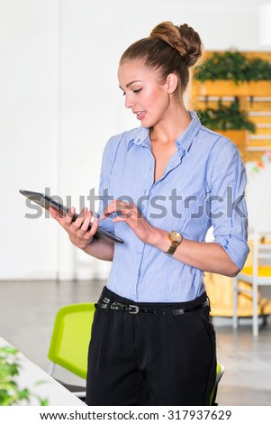Young businesswoman in modern bright office holding the tablet with a list of tasks. Business concept of office work