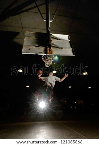 Basket and basektball player jumping with ball and aiming at basket with lights turned on at night