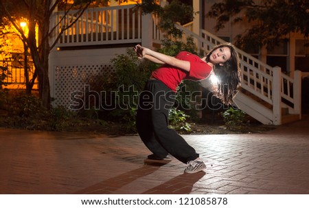 Girl doing a breakdance move at night on brick floor in urban setting, wearing a red t-shirt