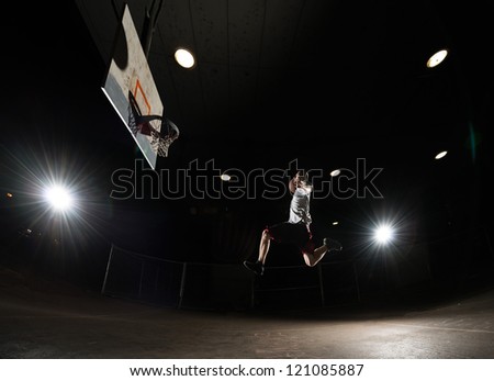 Basketball player at night jumping and aiming at hoop with lights on