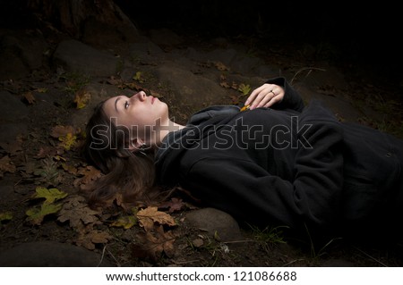 Attractive woman enjoying nature lying on her back in darkness lost in thought thinking deeply amongst fallen autumn leaves with copyspace