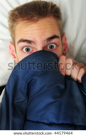 This white Caucasian young adult teenage man hides under his blankets and covers because he is scared of the spooky things that go bump in the night.