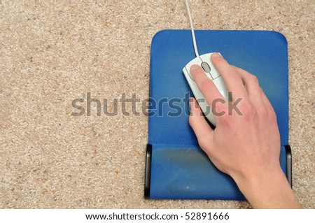 Hand on a mouse on a blue mouse pad on a tan carpet