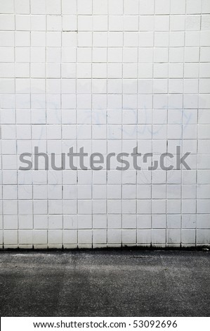 Tiled wall with a blank white bricks and gray spray painted graffiti.