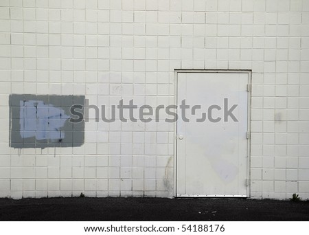 Tiled wall with a blank white door and gray spray paint covering graffiti.