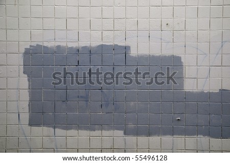 Tiled wall with a blank white bricks and gray spray painted graffiti.