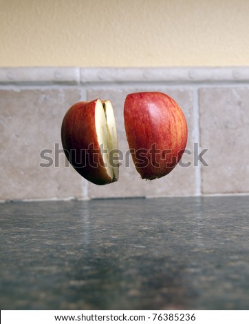 Red apple being cut in half with a sharp knife being held up by one single toothpick
