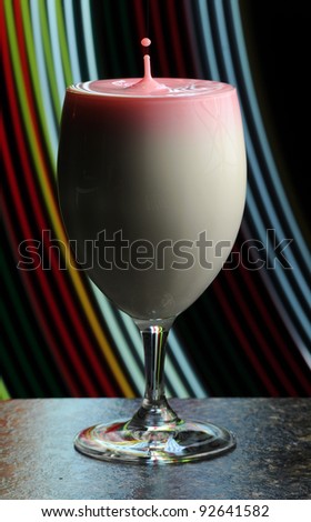 Abstract shot of a wine glass filled with milk and a splashing high speed droplet coming out of the top.