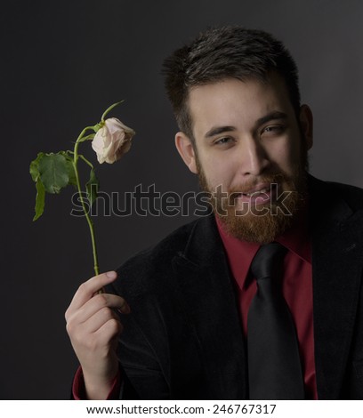 Close up Smiling Handsome Goatee Man in Formal Attire Holding Withered White Rose While Looking at the Camera. Captured on Gray Background