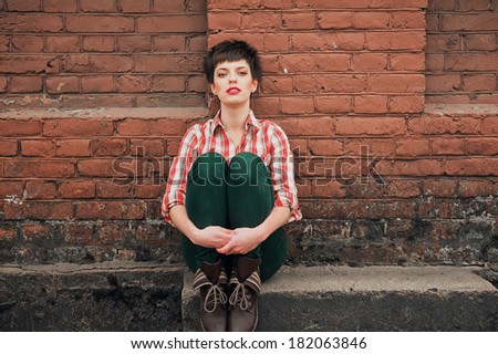 Young woman plaid shirt jeans near brick wall. Looking into the camera.