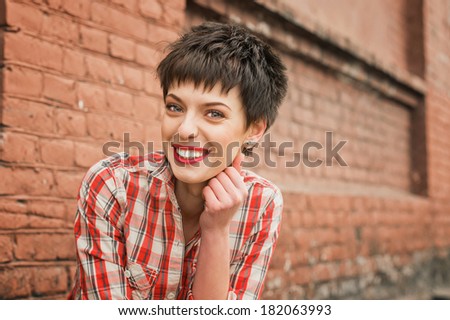 Girl smiling friendly. Young woman plaid shirt jeans near brick wall. Looking into the camera.