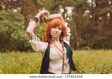 Redhead hippie walks in summer forest. Young woman with long hair in a long skirt and blouse in Boho style. Photo of romantic girl in national dress.