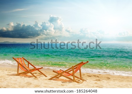 Two lounge chairs on the beach, clouds and sun