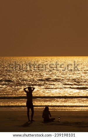 Boat silhouette in the golden sky and ocean. People stand on the shore.