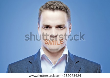 Serious young man without a mouth on a blue background with the words: Smile