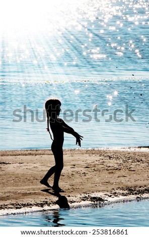 Silhouetto of a little girl in counter light on a river bank