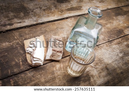 Bottle and glass of moonshine or vodka on the table, bread with lard