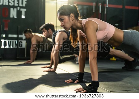 Group of athletic people men and woman with ponytail and gloves workout together. Doing plank for strenght and strong abs musclesin gym for healthy and sporty lifestyle. Sports activity training class