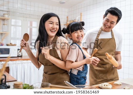 Asian happy family stay at home in kitchen spend time together baking bakery and foods. little kid with parents, father and mother dancing and laughing, enjoy parenting activity relationship in house.