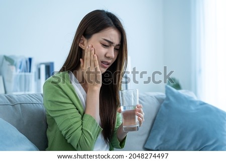 Asian beautiful woman feel terrible toothache after drink cold water. Attractive female sit on sofa in living room touching cheek, feel hurt and suffering from sensitive tooth ache, pain and cavities. Stock foto © 