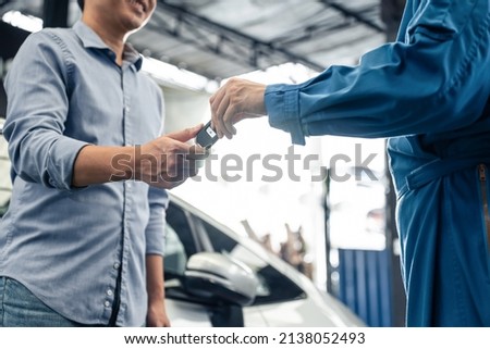 Asian automotive mechanic repairman handing car remote key to client. Vehicle service manager give the key back to car owner after successful of checking and maintenance car engine in mechanics garage Foto stock © 