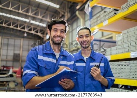 Portrait of two male industrial worker working in manufacturing plant. Young handsome male industry factory engineer wear helmet and processes order and product at manufactory warehouse with happiness Stockfoto © 