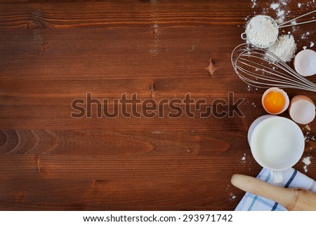 Ingredients for baking dough including flour, eggs, milk, whisk and rolling pin on wooden rustic background, empty space for text, top view, toning