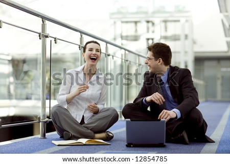 Business couple portrait - young man and woman working together on the floor of modern office corridor