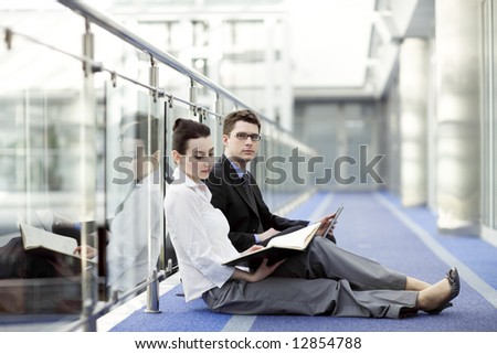 Business couple portrait - young man and woman working together on the floor of modern office corrdor