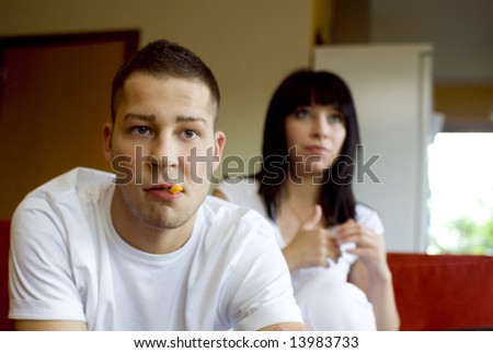 Disgusted man with chips in his mouth watching tv with his girfriend