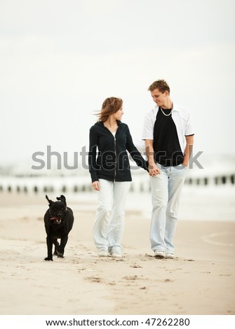 two young people walking on the beach holding tight with dog