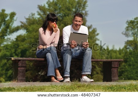 couple in park sitting together on bench working reading computer
