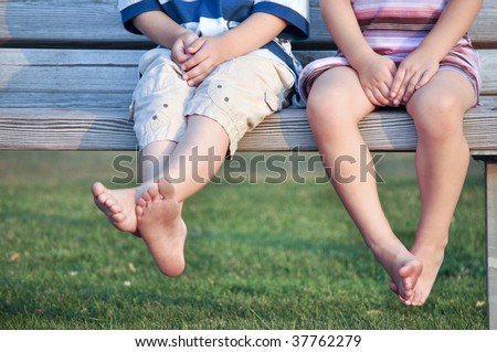 legs of barefoot boy and girl sitting on bench