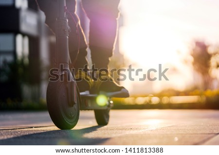 Close up of man riding black electric kick scooter at cityscape at sunset