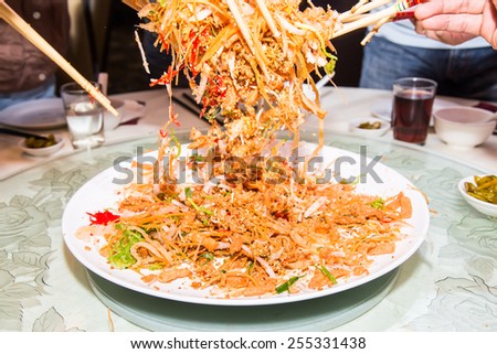 A group of people mixing and tossing Yee Sang dish with chop sticks. Yee Sang is a popular delicacy taken during Chinese New Year, believed to bring good fortune and luck
